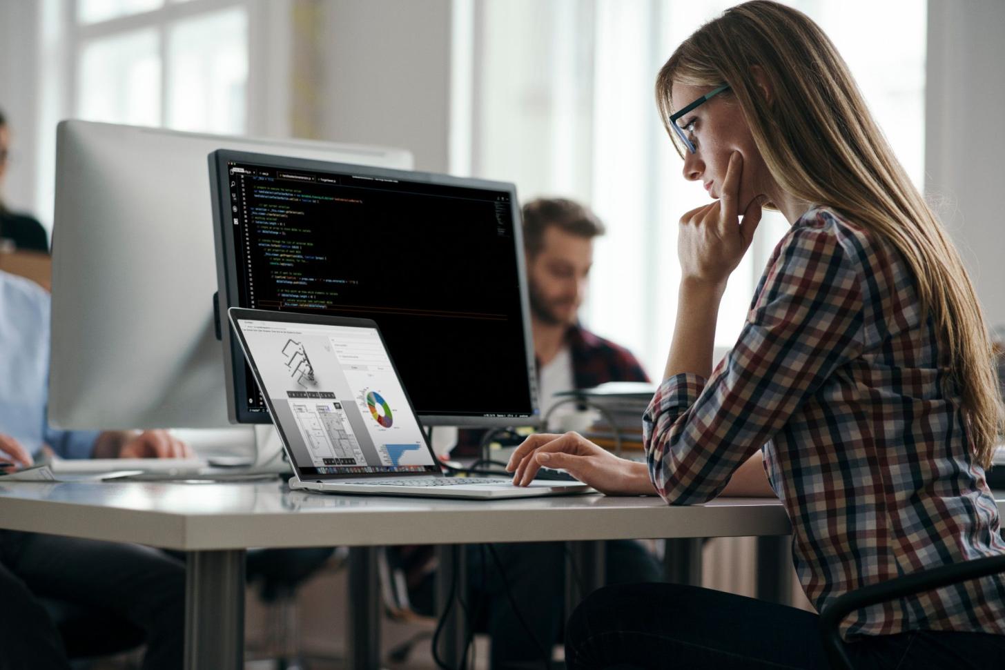 A developer in a plaid shirt looks at a laptop in an office. 
